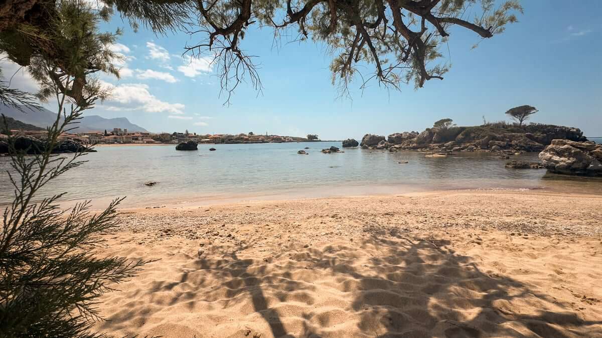 Sandy beach in the Mani with calm water, rocks and tree shade