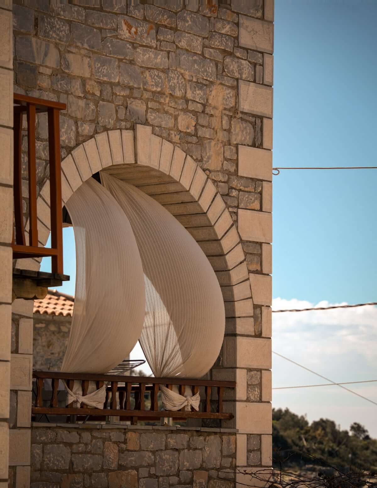 Stone house in the Mani with an arched balcony, billowing white curtains and sea views