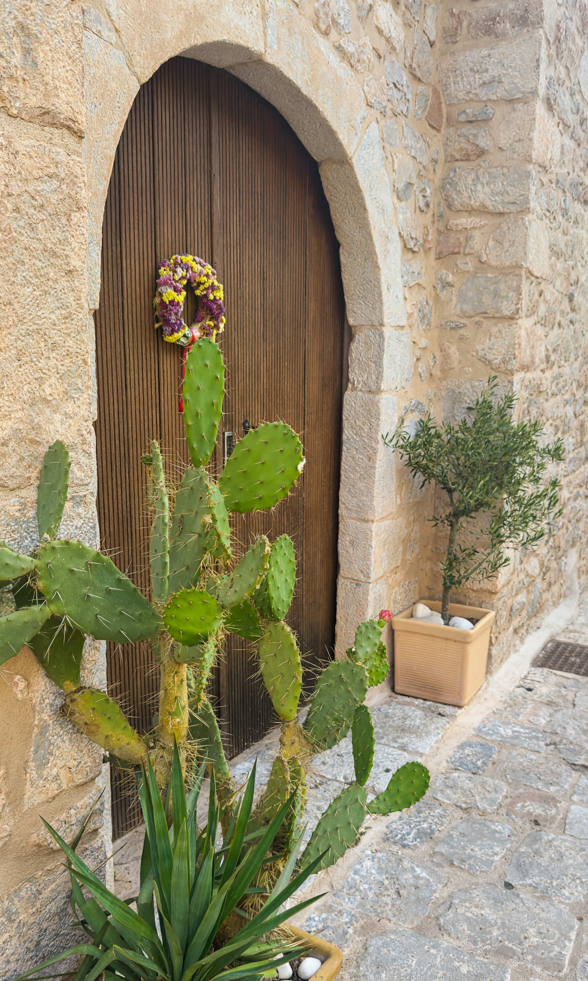 Traditional stone entrance in the Mani with a wooden door, flower wreath and Mediterranean plants